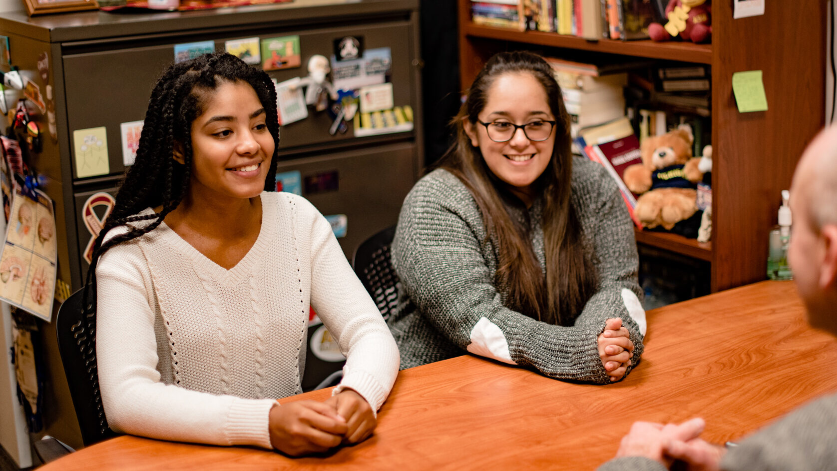 Two On-Campus students sitting at a Professor's desk.