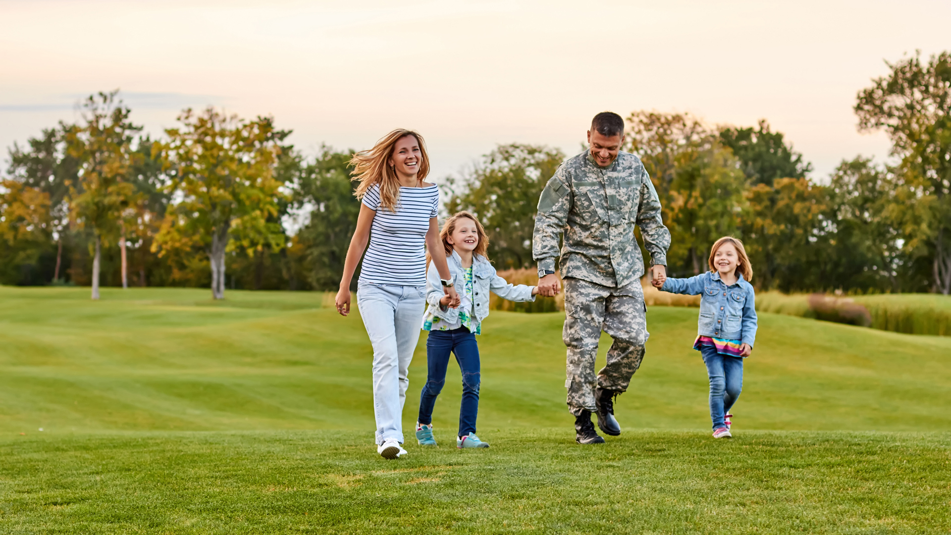Military student family walking hand in hand through a field of grass.