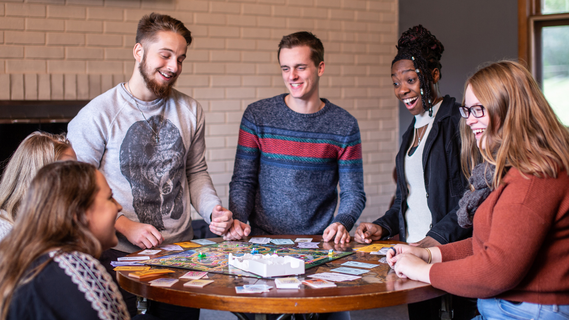 A diverse group of On-Campus Grace Students around a table playing a board game.