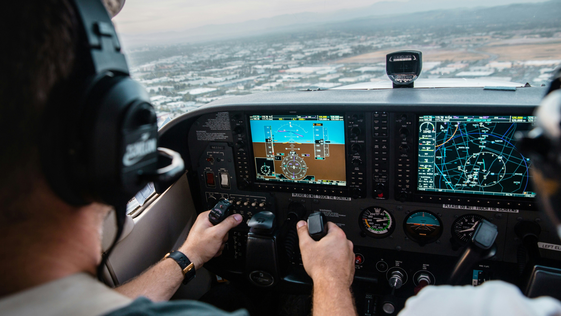 A view of a cockpit showing the pilot flying the plane over a city.