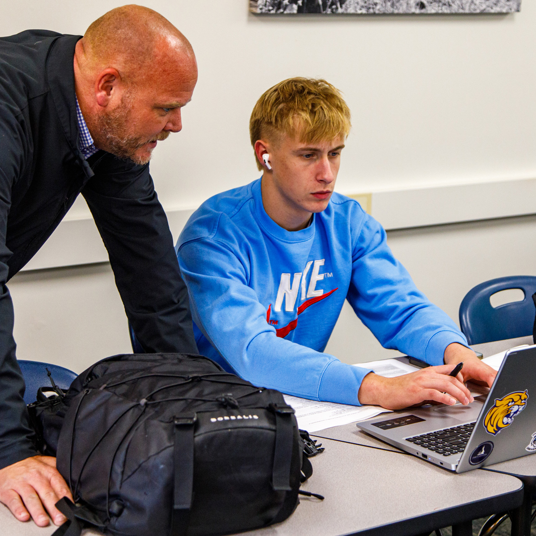 A Grace Professor helping a student in a classroom.